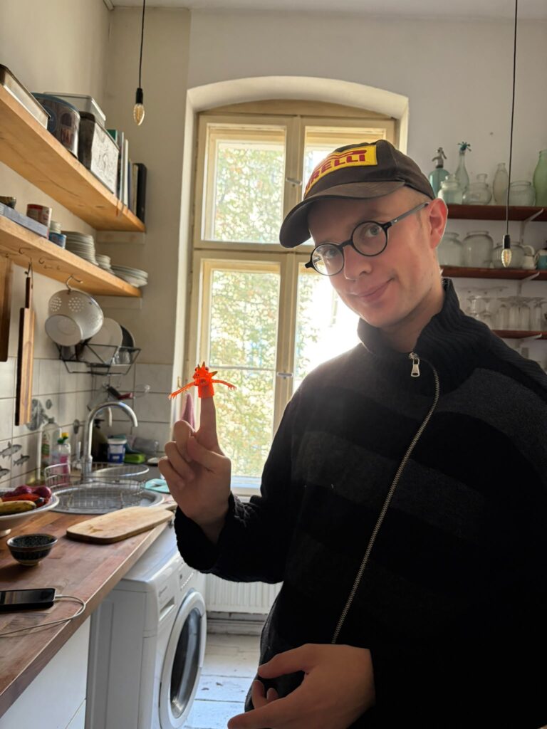 Hugh Morris standing in front of a kitchen window with a small plastic puppet on his finger